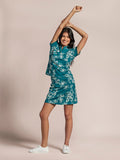 Teal solid polo shirt, short sleeves, front view, woman raising arms against beige background.