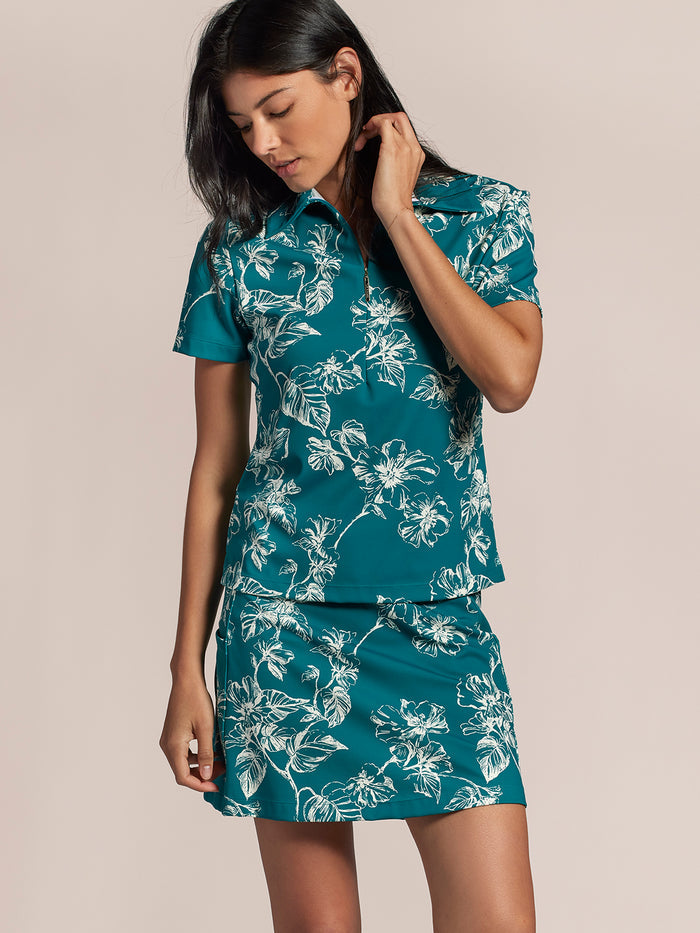 Teal floral-print short-sleeve polo shirt and matching skirt; woman touching collar.