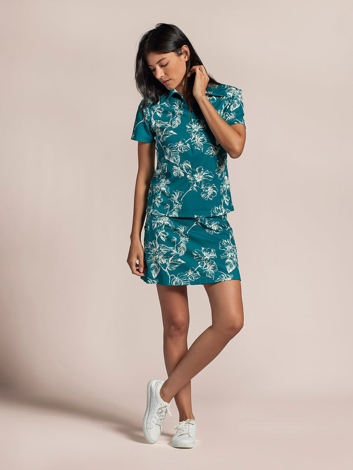 Teal floral skort, front view, worn with white sneakers; moisture-wicking and UPF fabric.