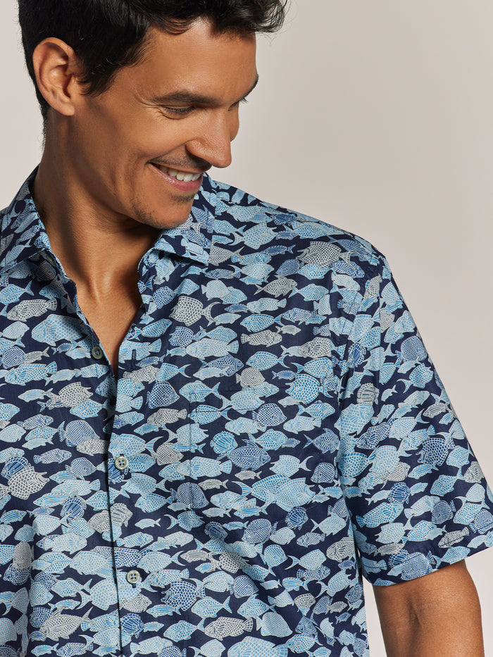 Blue Hawaiian-print short-sleeve cotton shirt, front view on smiling man against plain background.