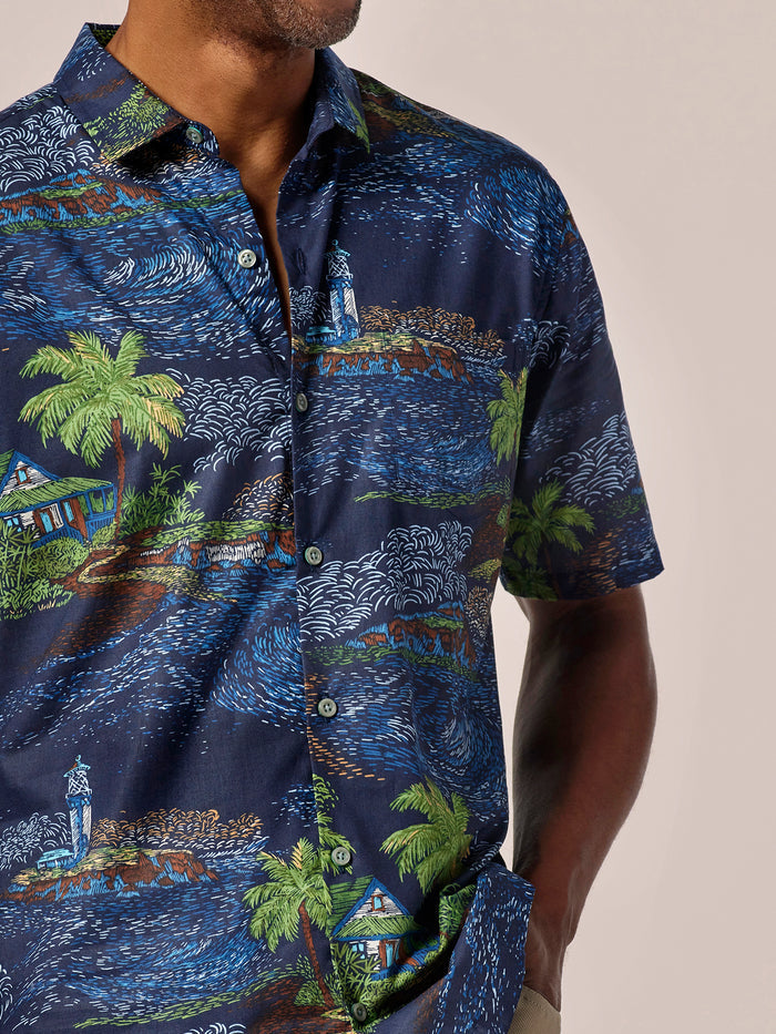 Blue palm tree and hut-print cotton shirt, short sleeves, front view, hand in pocket.