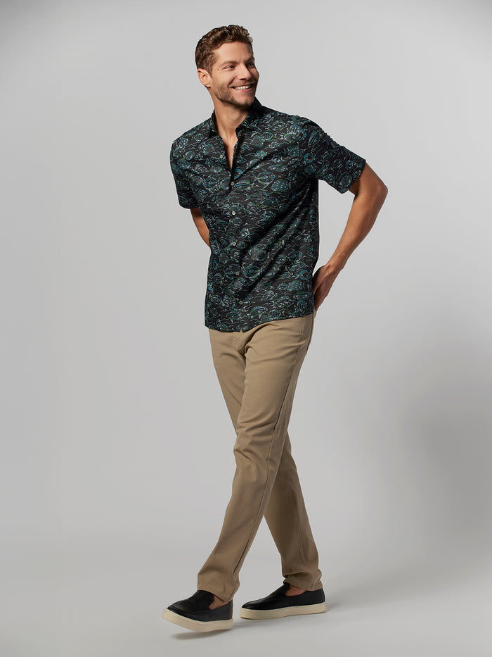 Dark patterned short-sleeve shirt, brown Honolulu pants, and slip-ons, front walking view.