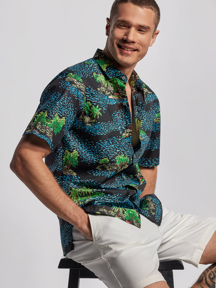 Blue and green tropical print short-sleeve shirt with matching white shorts, seated front view.