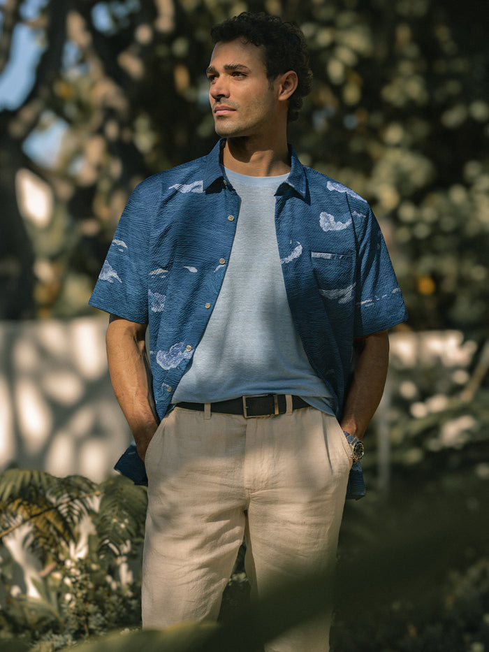 Blue cloud-pattern short-sleeve shirt, polyester, hands in pockets, outdoor back-side view.