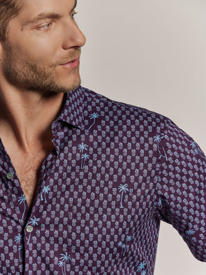 Purple short-sleeve shirt with white pineapple and blue palm tree print, side view.