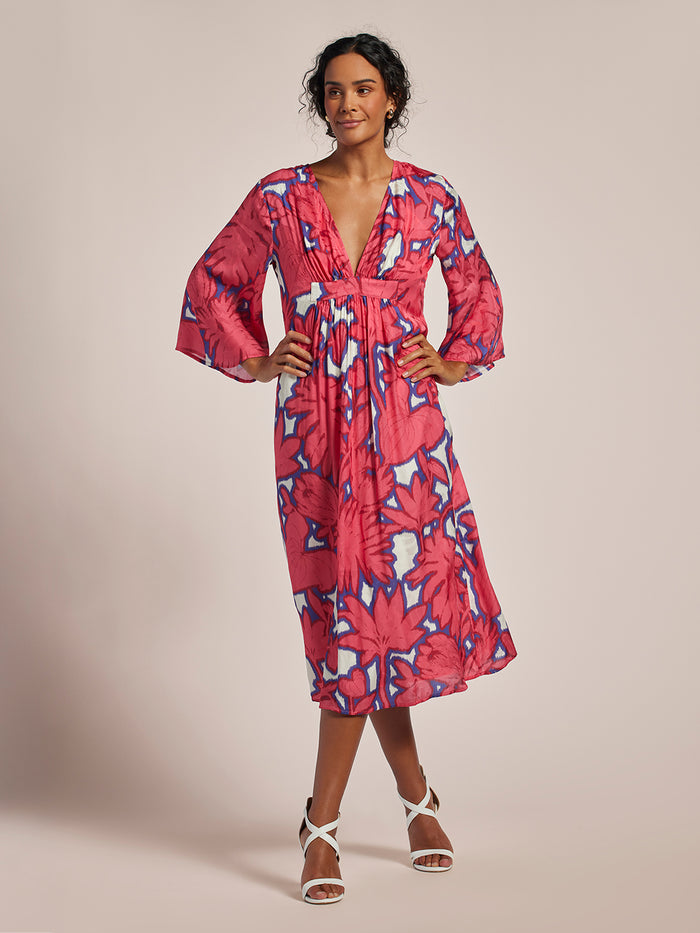 Pink floral-print midi caftan with v-neck, shown on model wearing white strappy heels, front view.