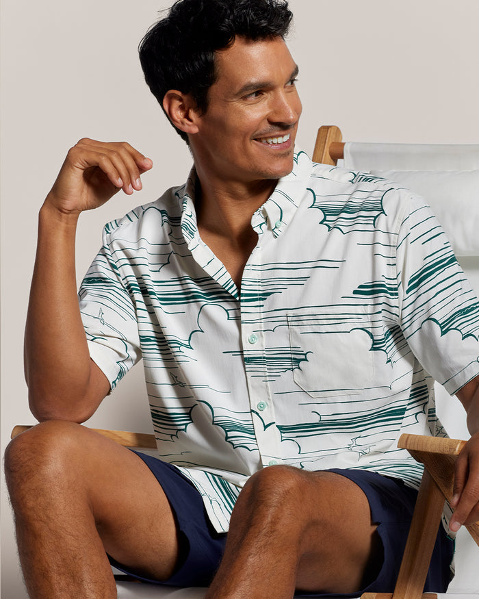 Light blue cloud-print short-sleeve shirt and navy shorts, seated front view in both images.