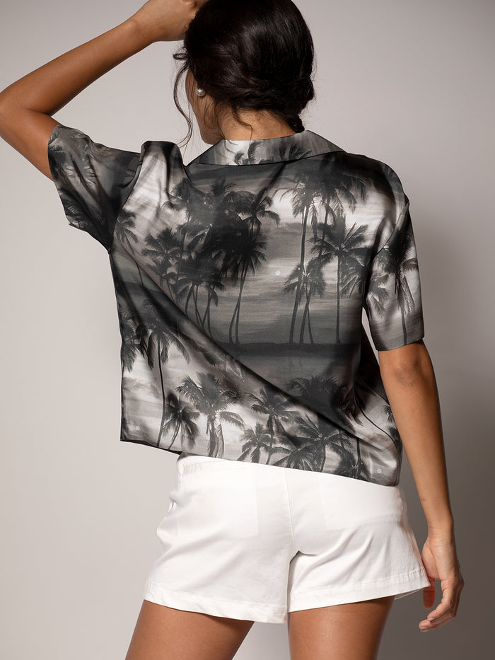 Black cabana-print sleeveless top floral cabana top and white shorts, back view, hand in hair.
