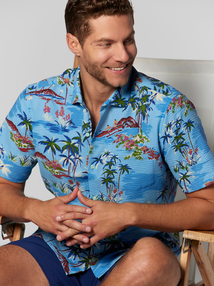 Man in blue palm-print Hawaiian short-sleeve shirt, clasping hands, front view.