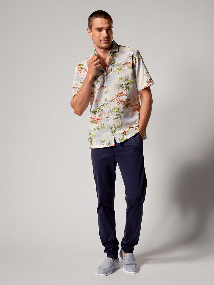 Cream and white island-print short-sleeve shirt with navy pants, front view.