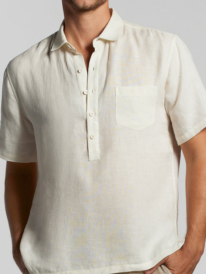 Cream solid linen half placket shirt, front view, model’s hands in pockets.