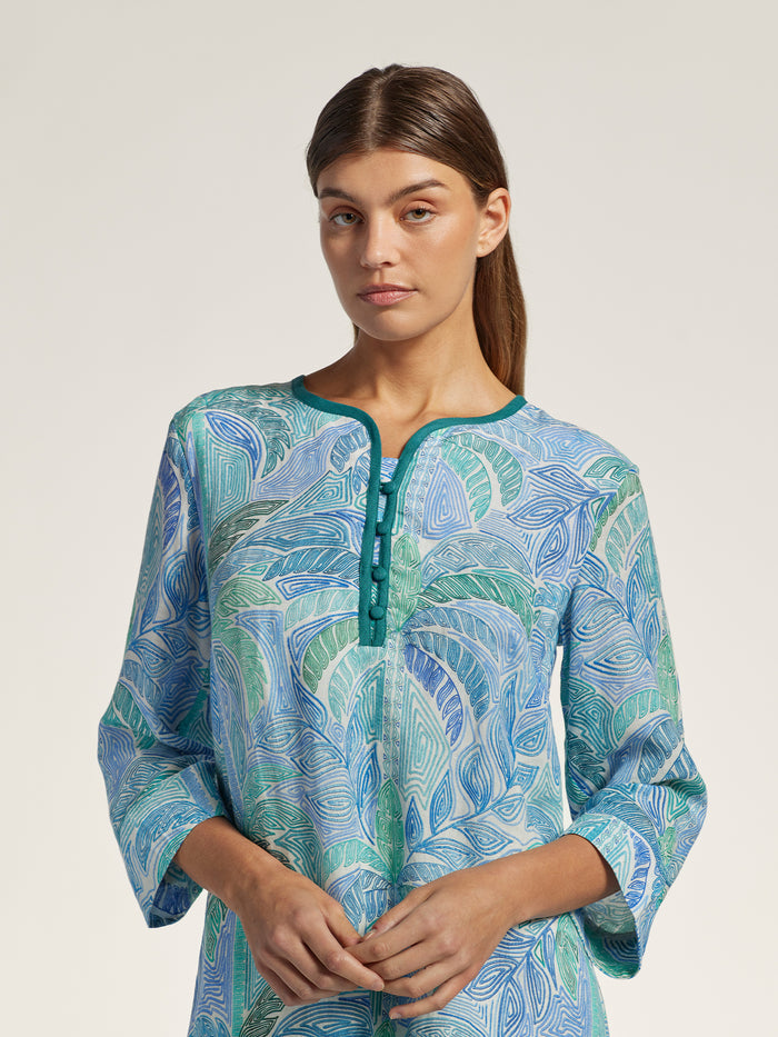 Woman wearing a blue and green patterned dress against a plain background