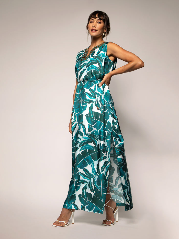 White and green leaf-print sleeveless maxi dress shown side and front view, paired with white heels.