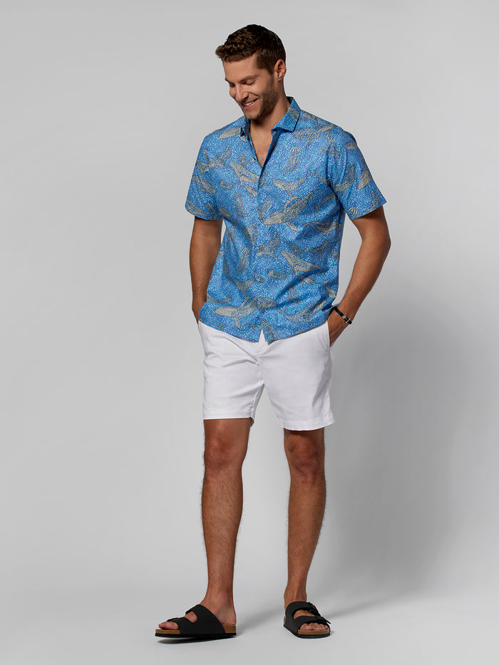 Blue multicolor mosaic-print short-sleeve shirt and white shorts, front view with hands in pockets.