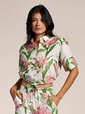 Cream and pink floral-print blouse and pants set, woman standing with hands in pockets.