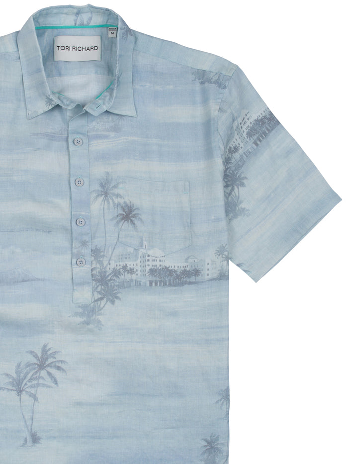 Light blue palm tree print linen shirt with half placket, four buttons, and chest pocket, front view.