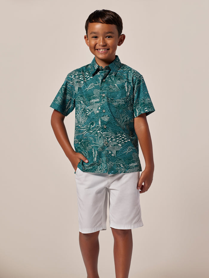 Boy in green tropical-print short-sleeve shirt and white shorts, standing front view.