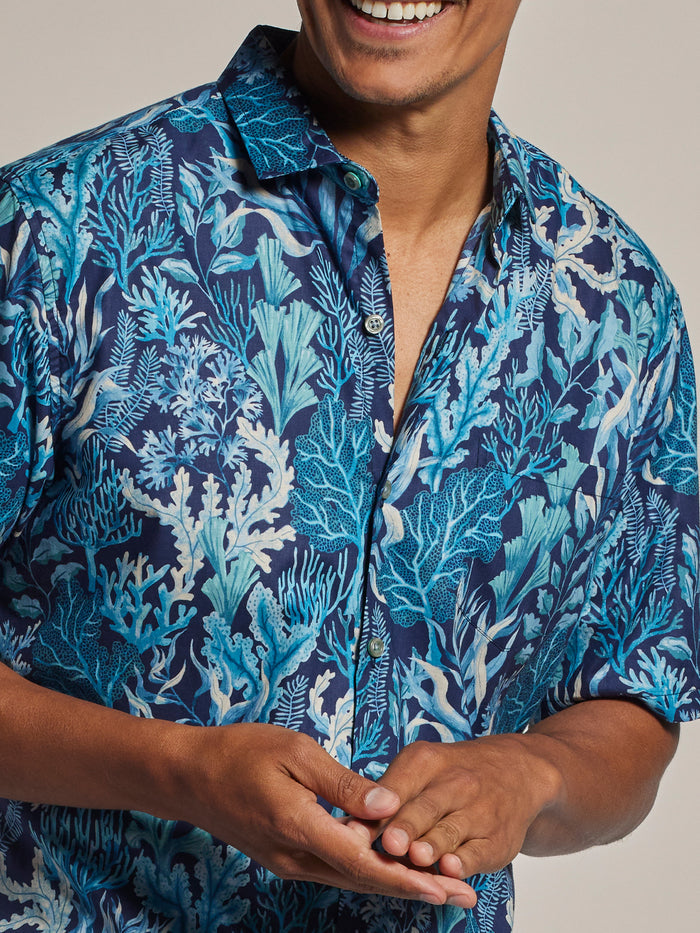 Blue tropical-print short-sleeve shirt, shoulders to waist, hands clasped.