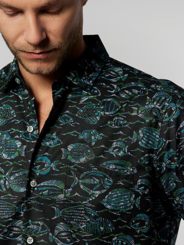 Image 1: Black cotton lawn shirt, blue-green fish print, partial front view. Image 2: Same shirt, man looking down.