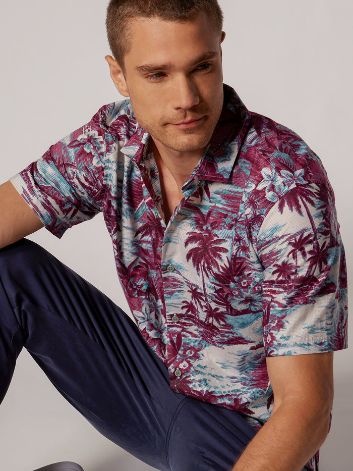 Light blue and white coast-print cotton lawn shirt with navy pants, seated side view.