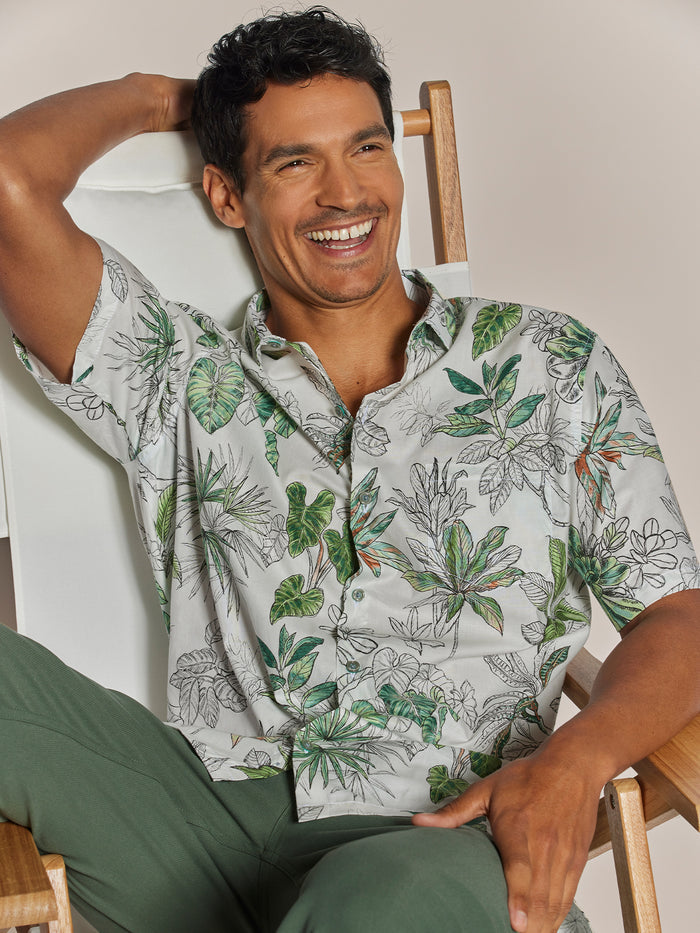 Smiling man in blue patterned short-sleeve shirt and green pants, front view.