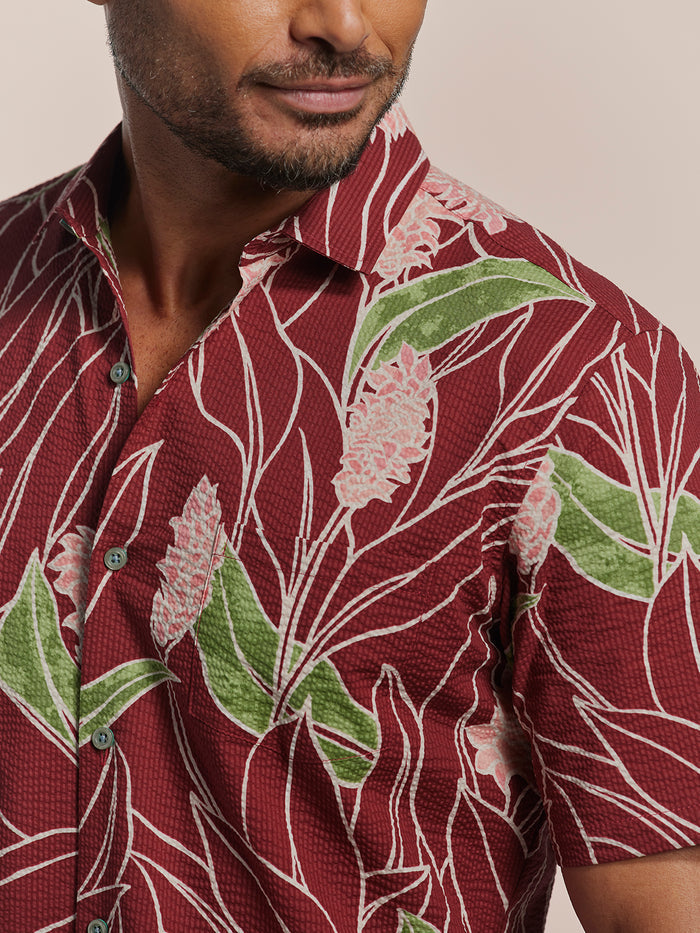 Red tropical floral-print short-sleeve cotton shirt with green leaves and pink flower print, Hawaiian-made, side view.