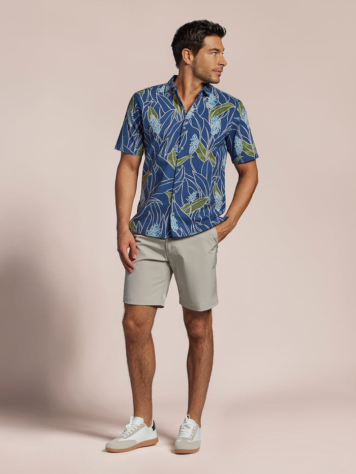 Blue short-sleeve shirt with green and light blue floral print and light gray shorts, full front view of a man.