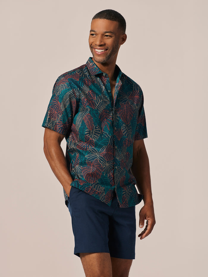 Man smiling, wearing a white shirt with black abstract outline print and navy shorts, front view.
