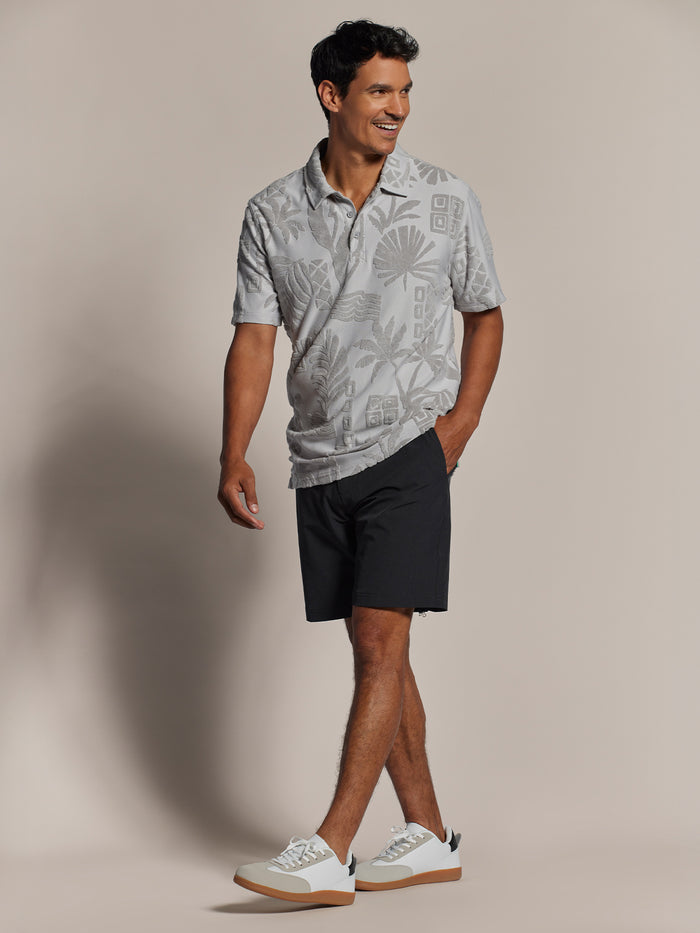 Grey tropical-print short-sleeve polo with black shorts, front view.