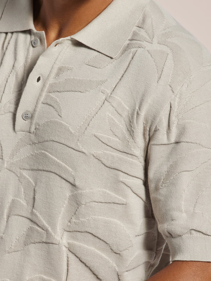 Light cotton jacquard polo with subtle palm leaf pattern and short sleeves, shown worn from the front.