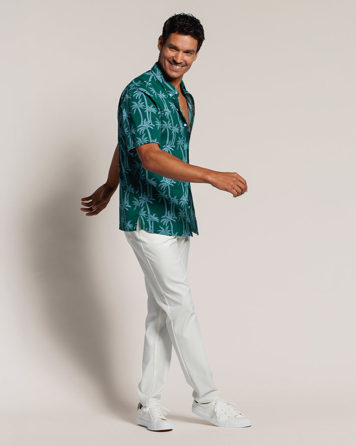 Green short-sleeve shirt with blue palm print; Tradewind Technology short-sleeve shirt with white pants, front walking view.