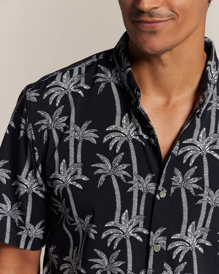 Black palm print short-sleeve Hawaiian shirt, man smiling, front view.
