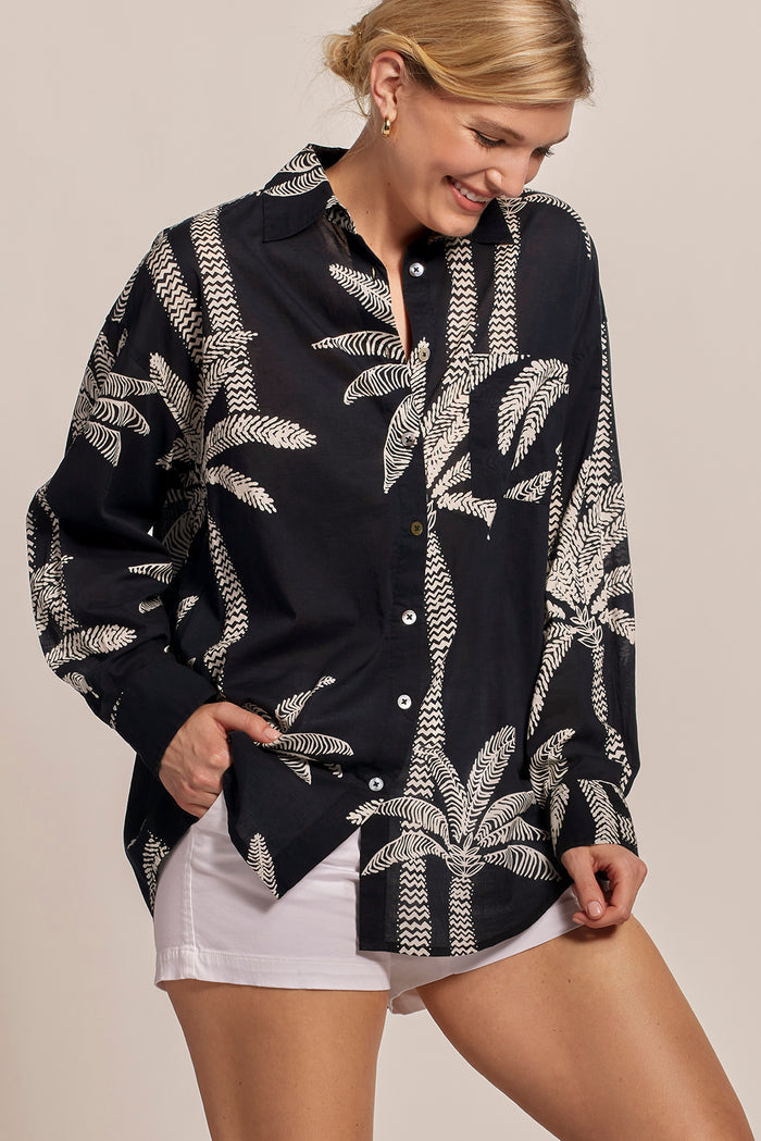 Black with white leaf-print short-sleeve top and white shorts, front view, hand in pocket.