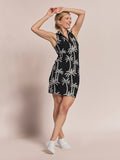 Woman in black sleeveless midi dress with palm print, arms raised, front view.