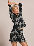 Black short-sleeve top with white palm print, front view with arms raised.