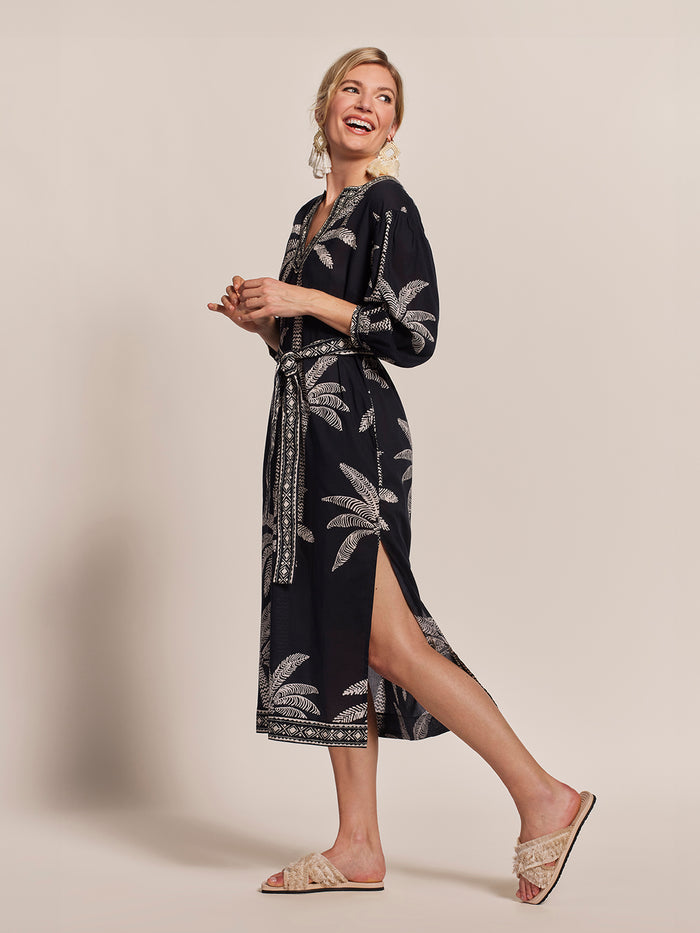 Black and white palm-print Trista caftan dress, side view, with beige sandals.