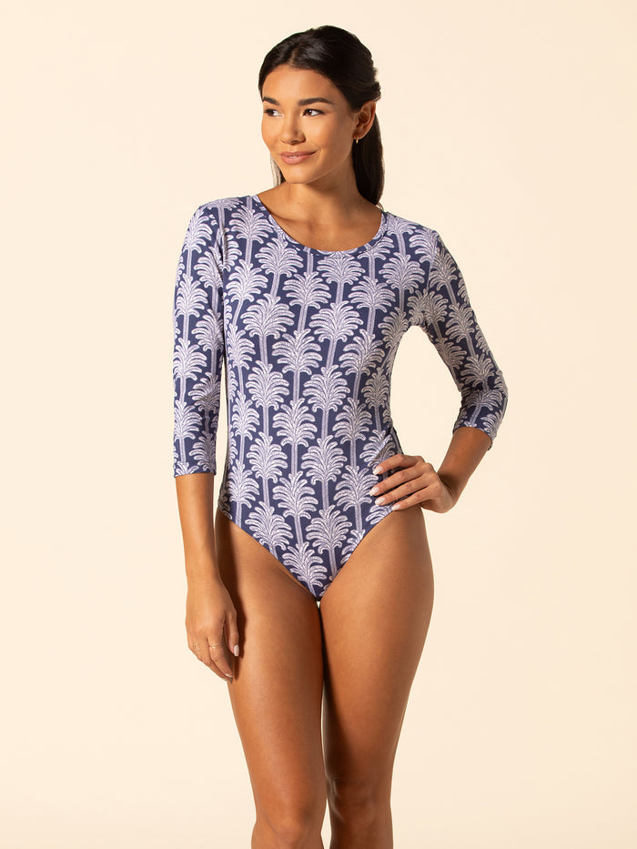 Palm leaf print jade navy bodysuit, three-quarter sleeves, woman posing with one hand on hip.