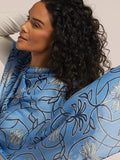 Woman with curly hair in white top, side view, wearing blue patterned silk scarf.