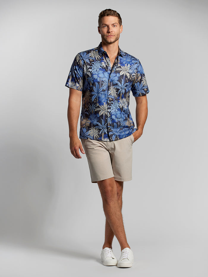 Blue, beige, and gray palm-print shirt with beige shorts; full-body view includes white sneakers.
