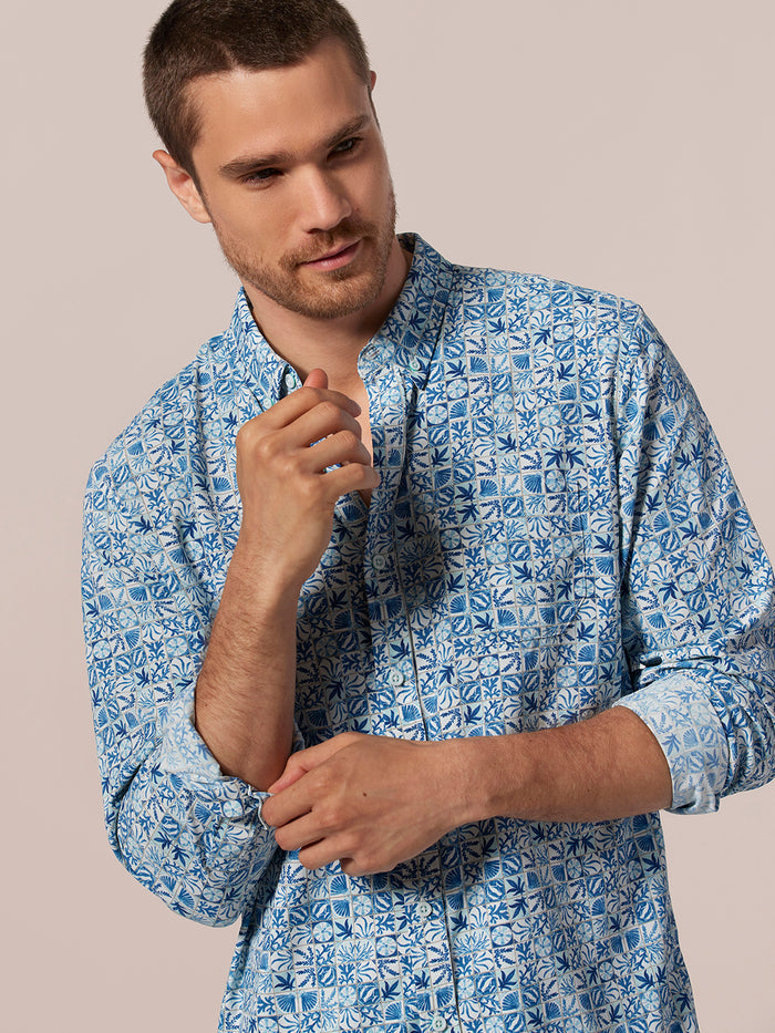 Blue and white geometric long-sleeve shirt, man looking down with one hand raised, front view.