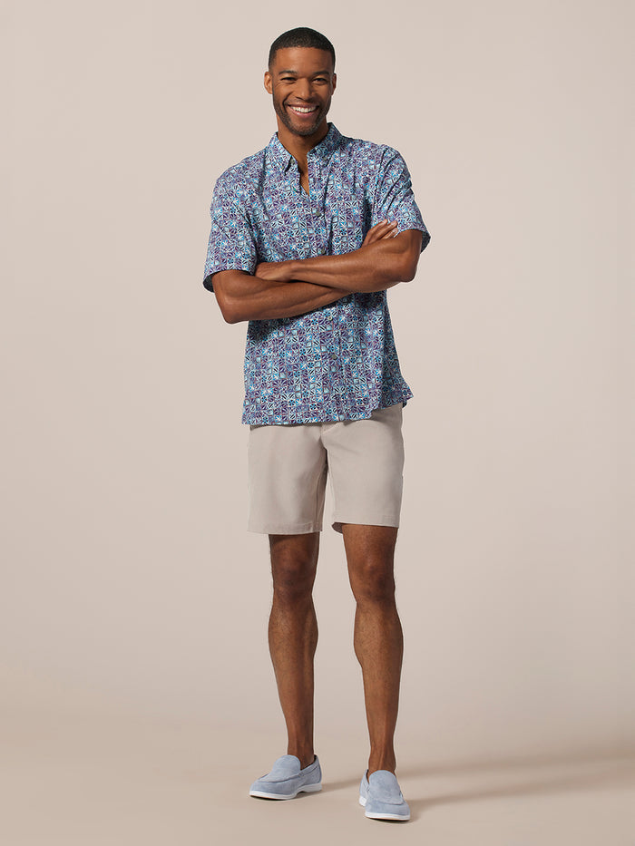 Blue floral short-sleeve shirt and beige shorts, front view with arms crossed.