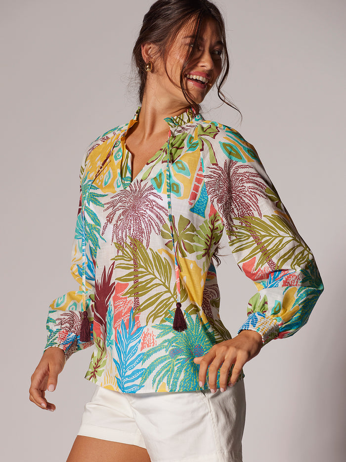 Tropical-print multicolor blouse and white shorts, side view of woman smiling.