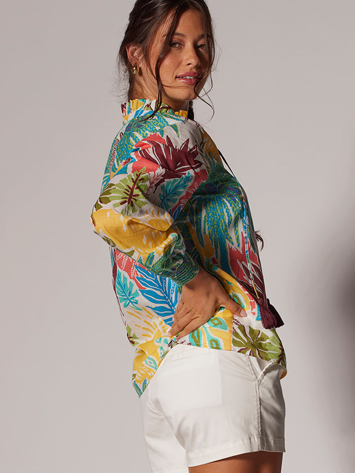 A model smiles in multi-colored tropical print blouse against plain background .