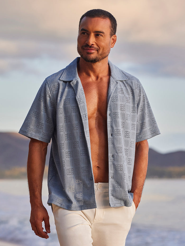 Blue and white tropical-print short-sleeve shirt with white pants, front view.