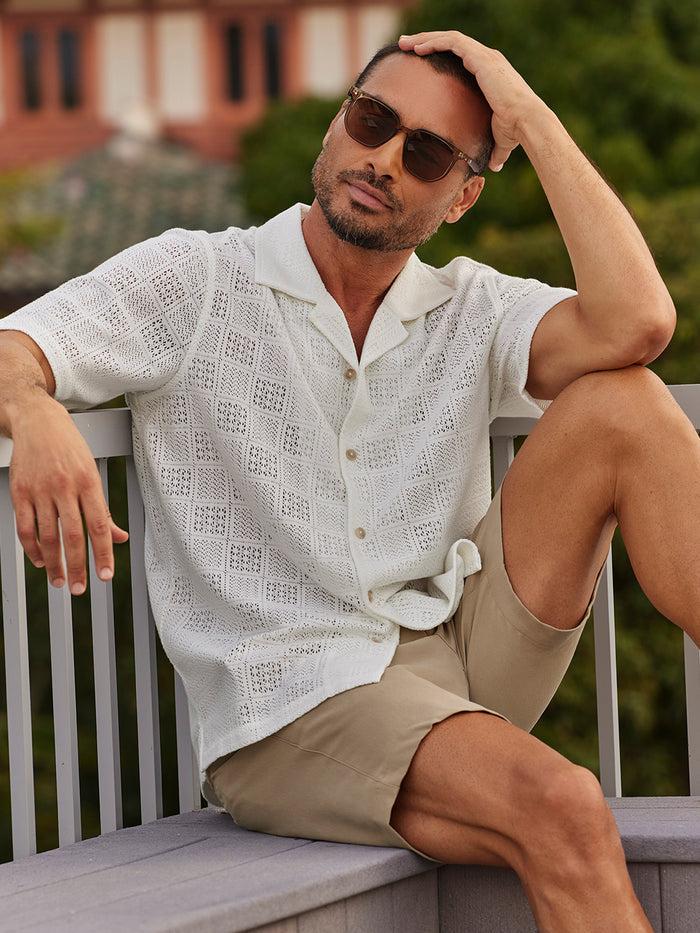 White tropical-print short-sleeve shirt with tan shorts, sitting outdoors, front view.