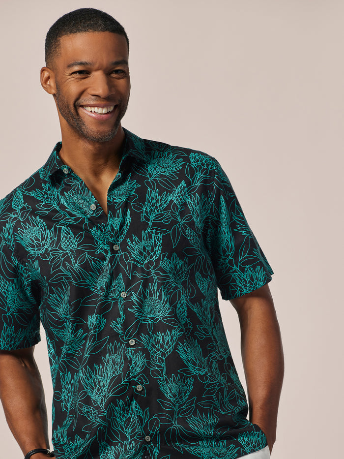Black Protea- with green floral print short-sleeve shirt, front view, worn by man against light background.