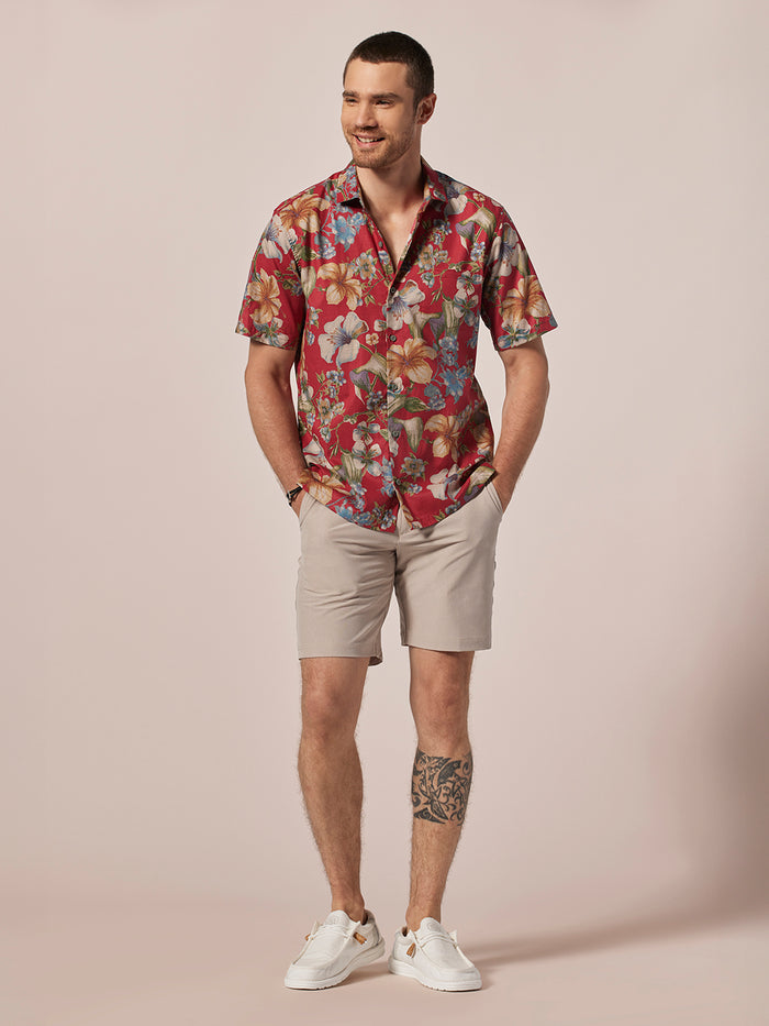 Red patterned short-sleeve Hawaiian shirt, beige shorts, white sneakers, hands in pockets.
