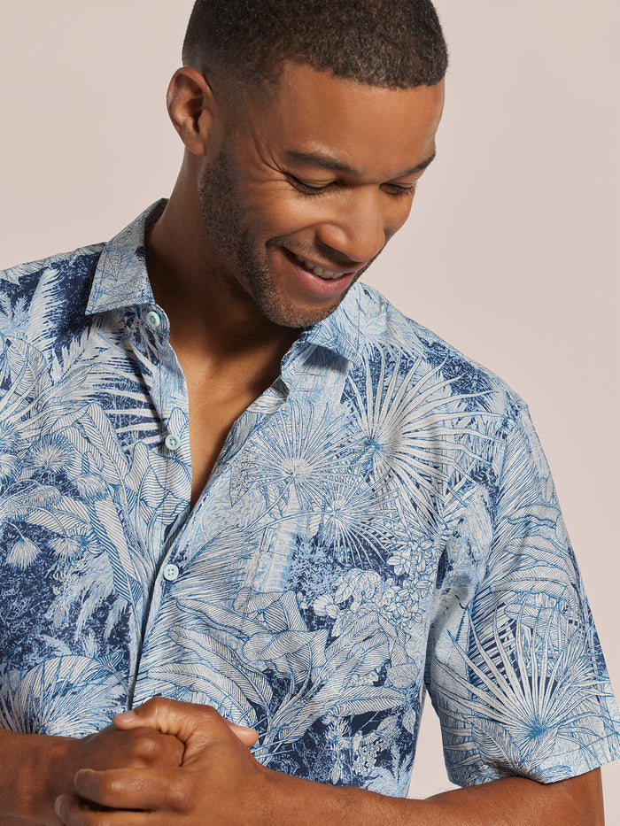 Blue solid cotton button-up shirt, front view on smiling man, plain background.