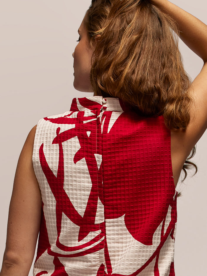 Red and white vintage-print dress, back view, woman with wavy brown hair, hand in hair.