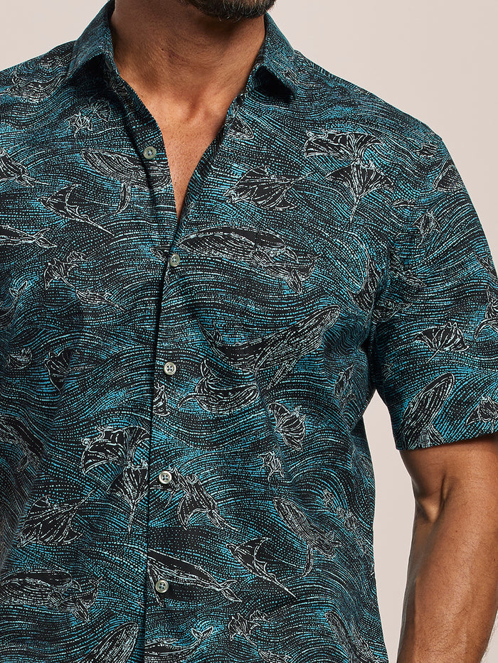 Blue short-sleeve shirt with black and gray abstract ocean and black whale print, shoulders-to-waist view of a close up photo of a man